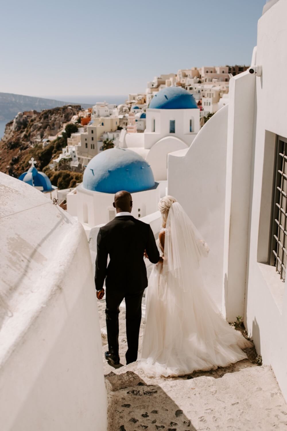 ethnic-destination-wedding-santorini-phosart-photographergreece-blue-domes-Bride-and-groom-first-look-love-kiss-flower-greek-island-1