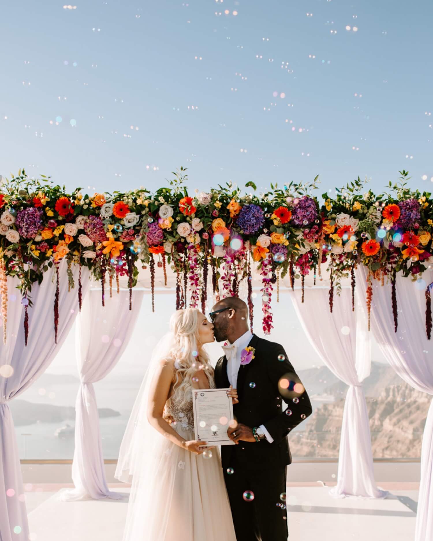 ethnic-destination-wedding-santorini-phosart-photographergreece-bubbles-Bride-and-groom-Ceremony-love-flower-decoration-love-kiss